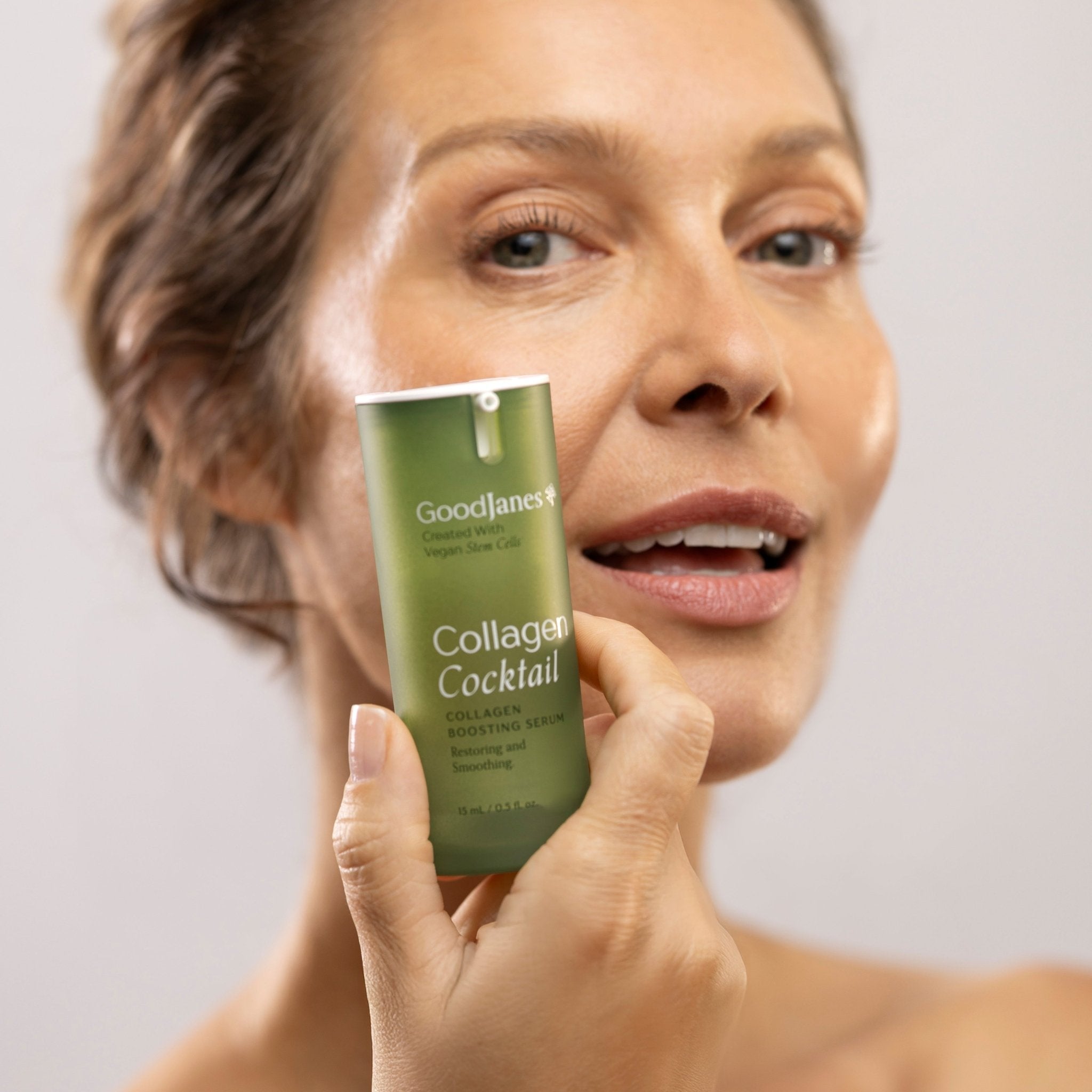 Woman holding a skincare product labeled 'Collagen Cocktail' by Good&Natured against a plain background