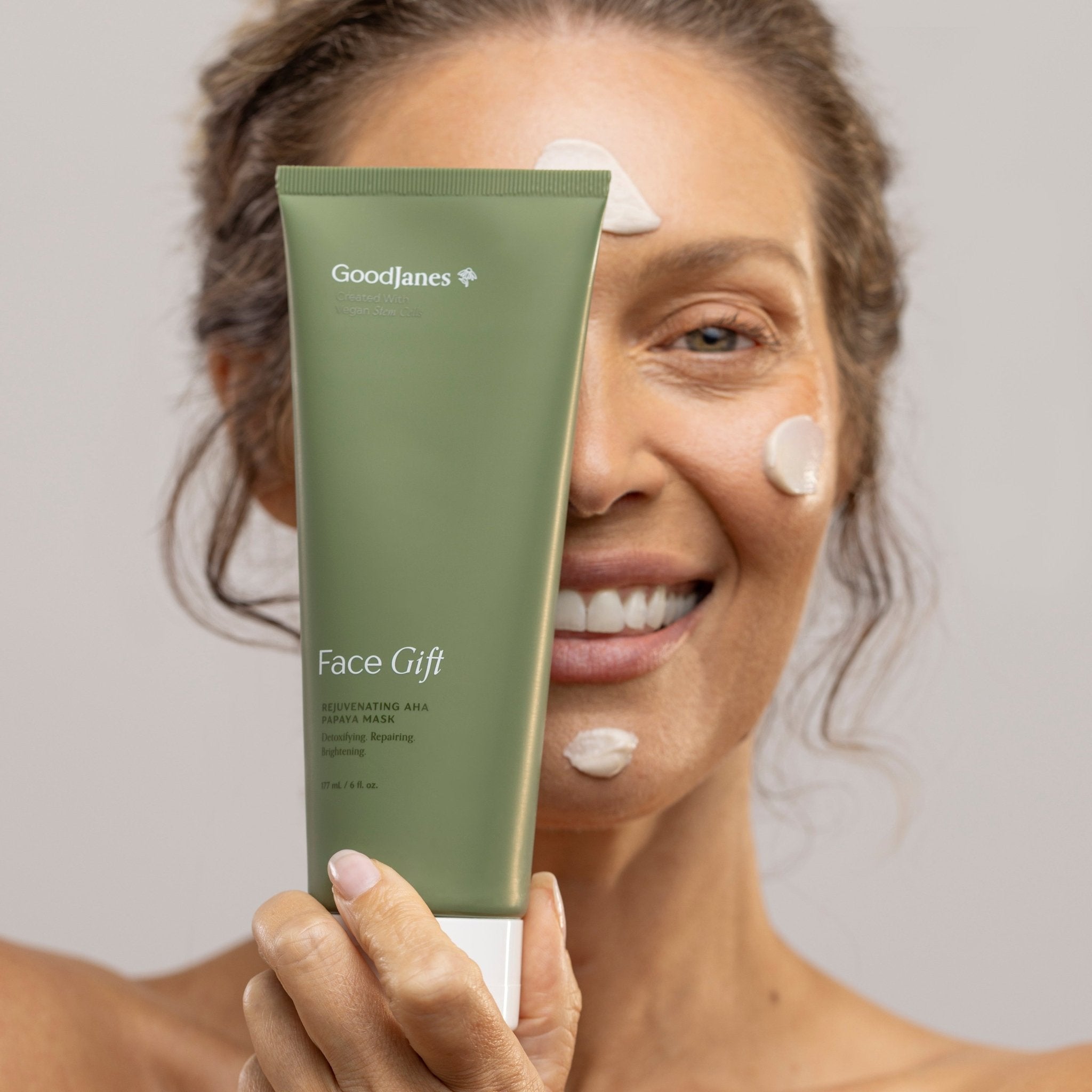 Woman holding a green skincare product with 'Goodlines' branding against a neutral background