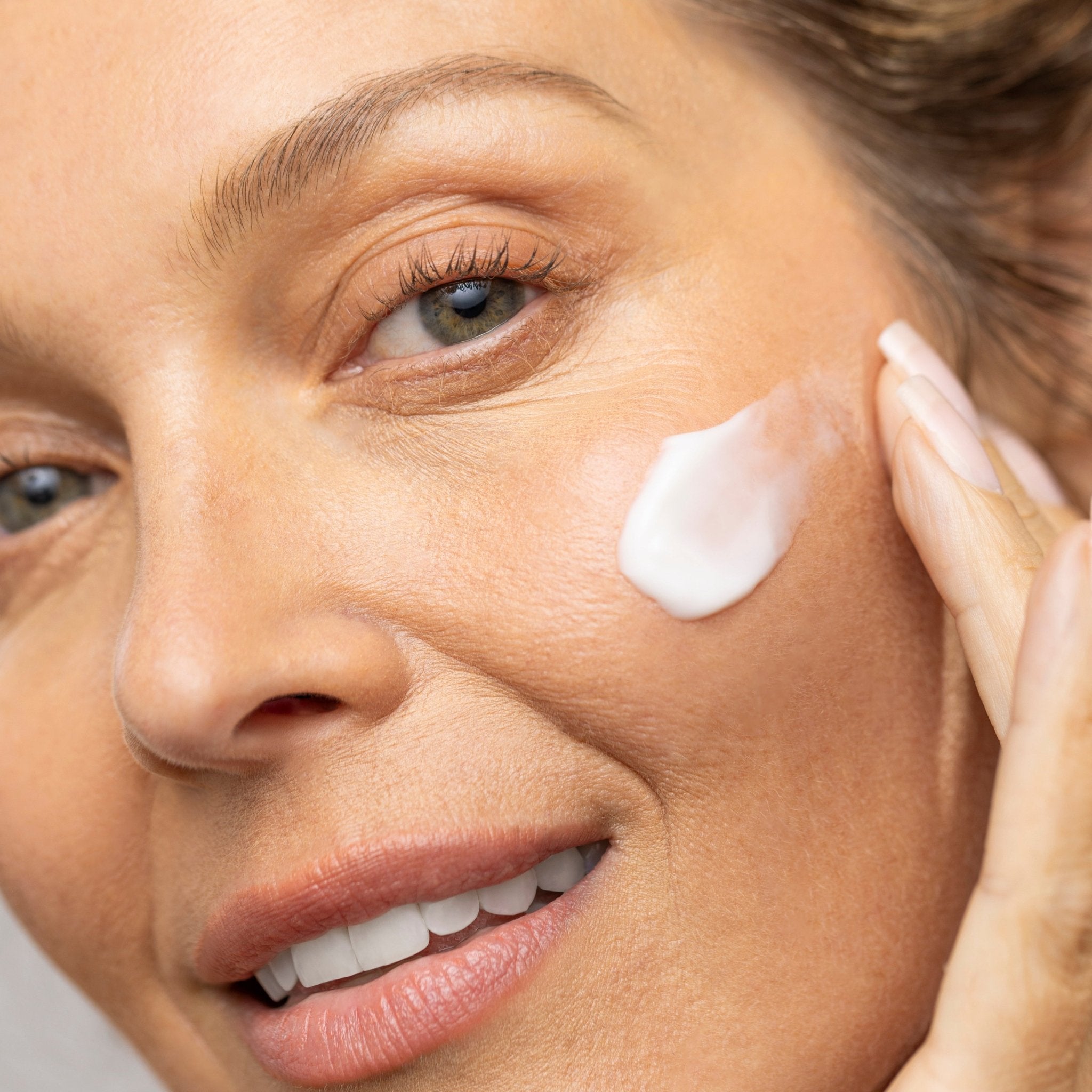 Woman applying cream to her face with a neutral background