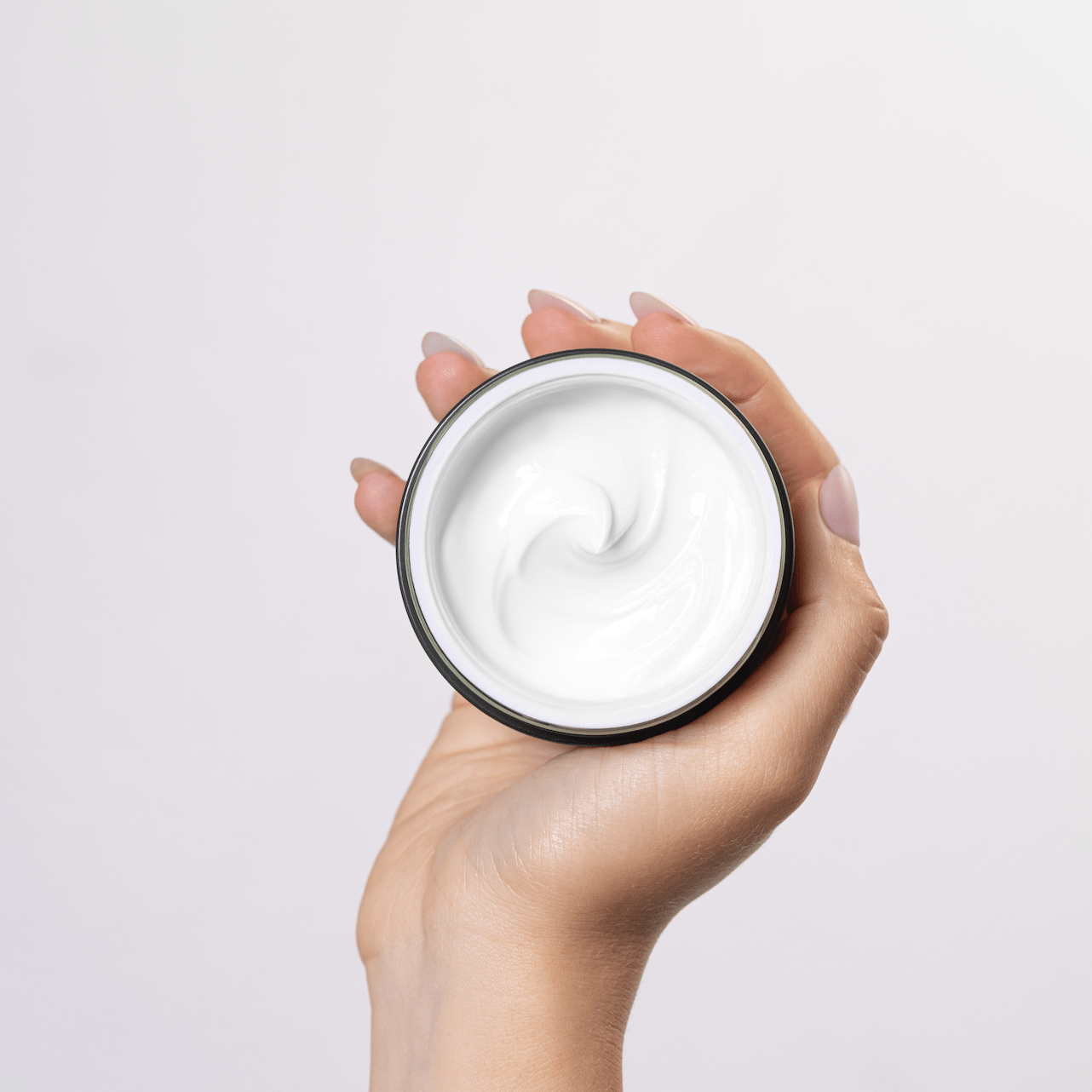Hand holding a jar of white cream against a light background