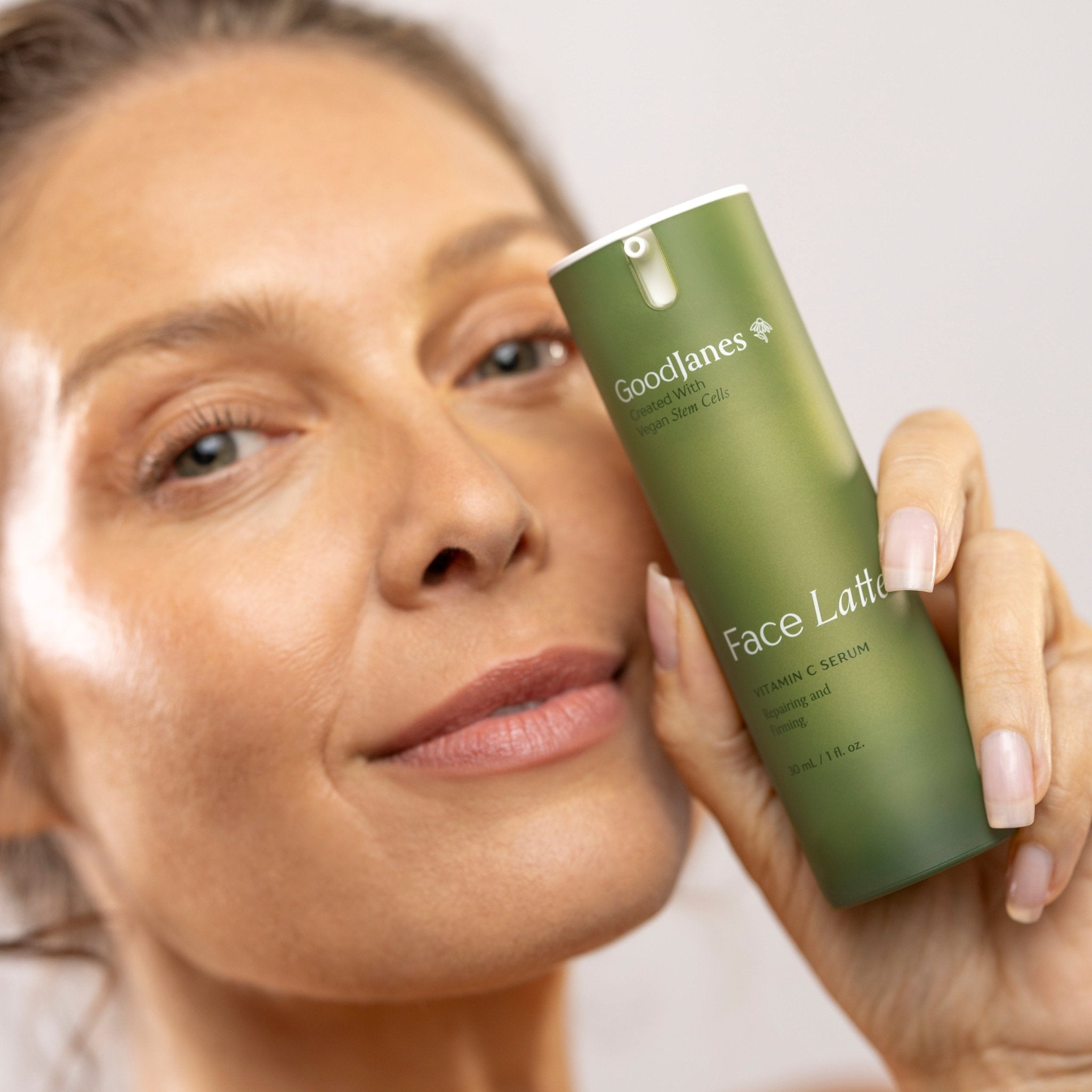 Woman holding a green skincare product labeled 'Goodlines' against a neutral background