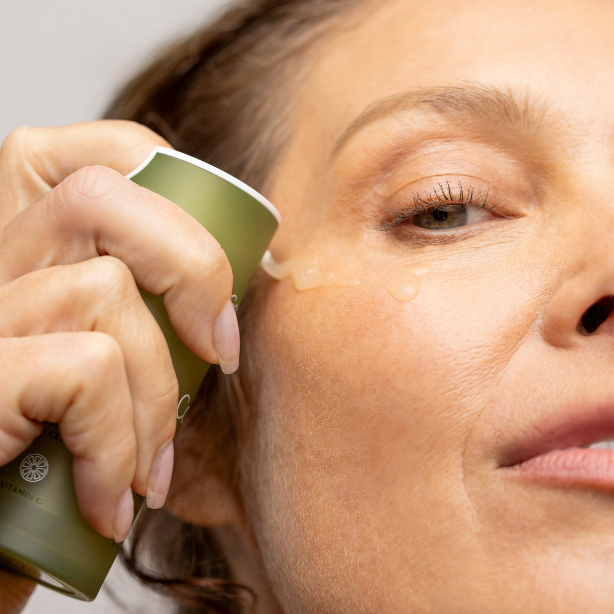 Woman applying a cosmetic product to her face with a green applicator.