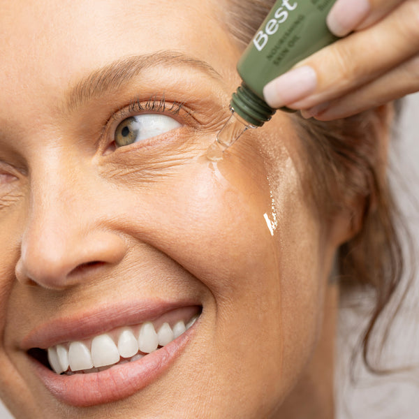 Woman applying a green bottle labeled 'Best Face Oil' to her face.