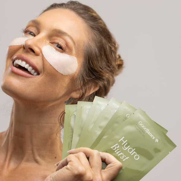 Woman with hydrogel patches on her face holding green packets labeled 'Hydro Burst'.