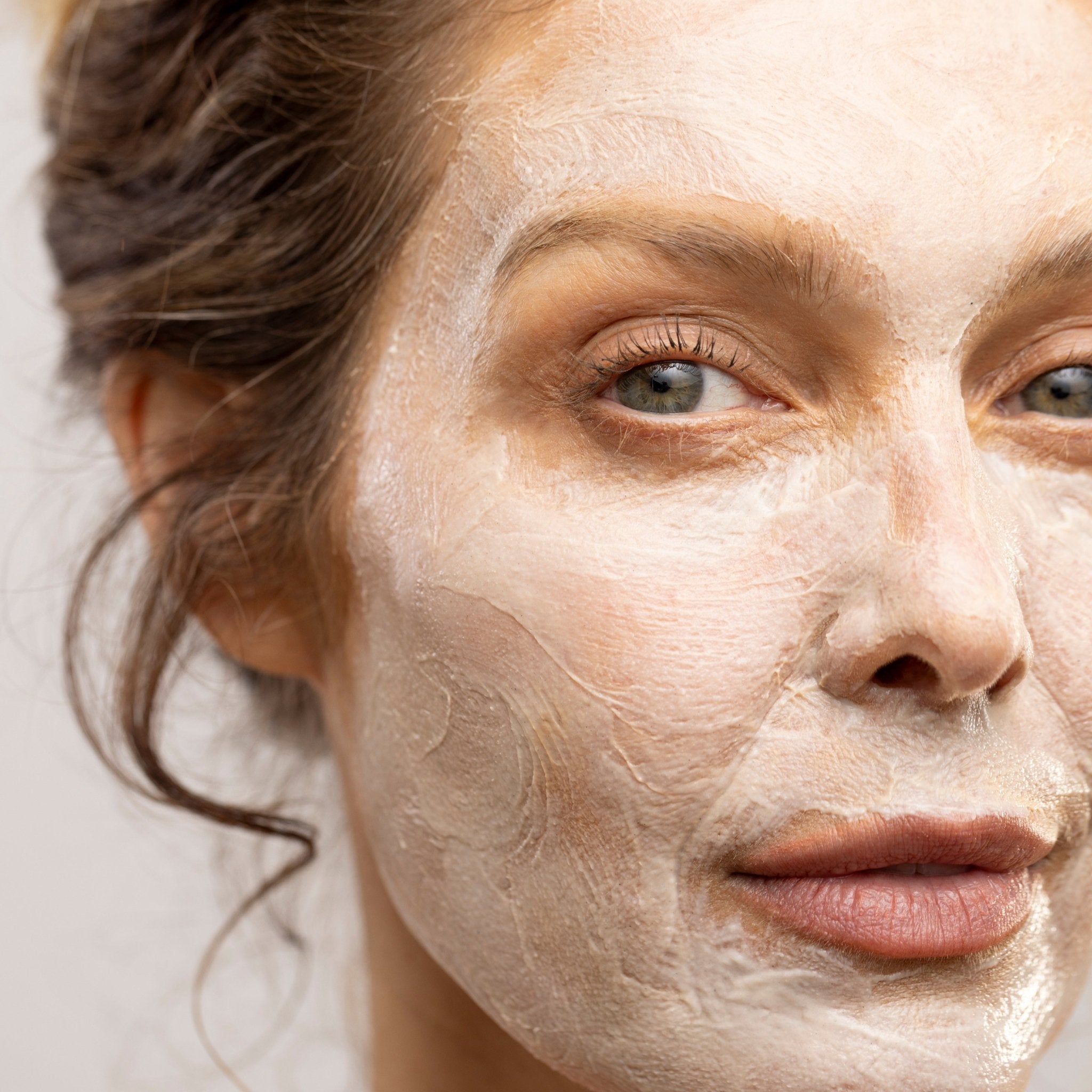 Woman with a clay mask on her face against a neutral background