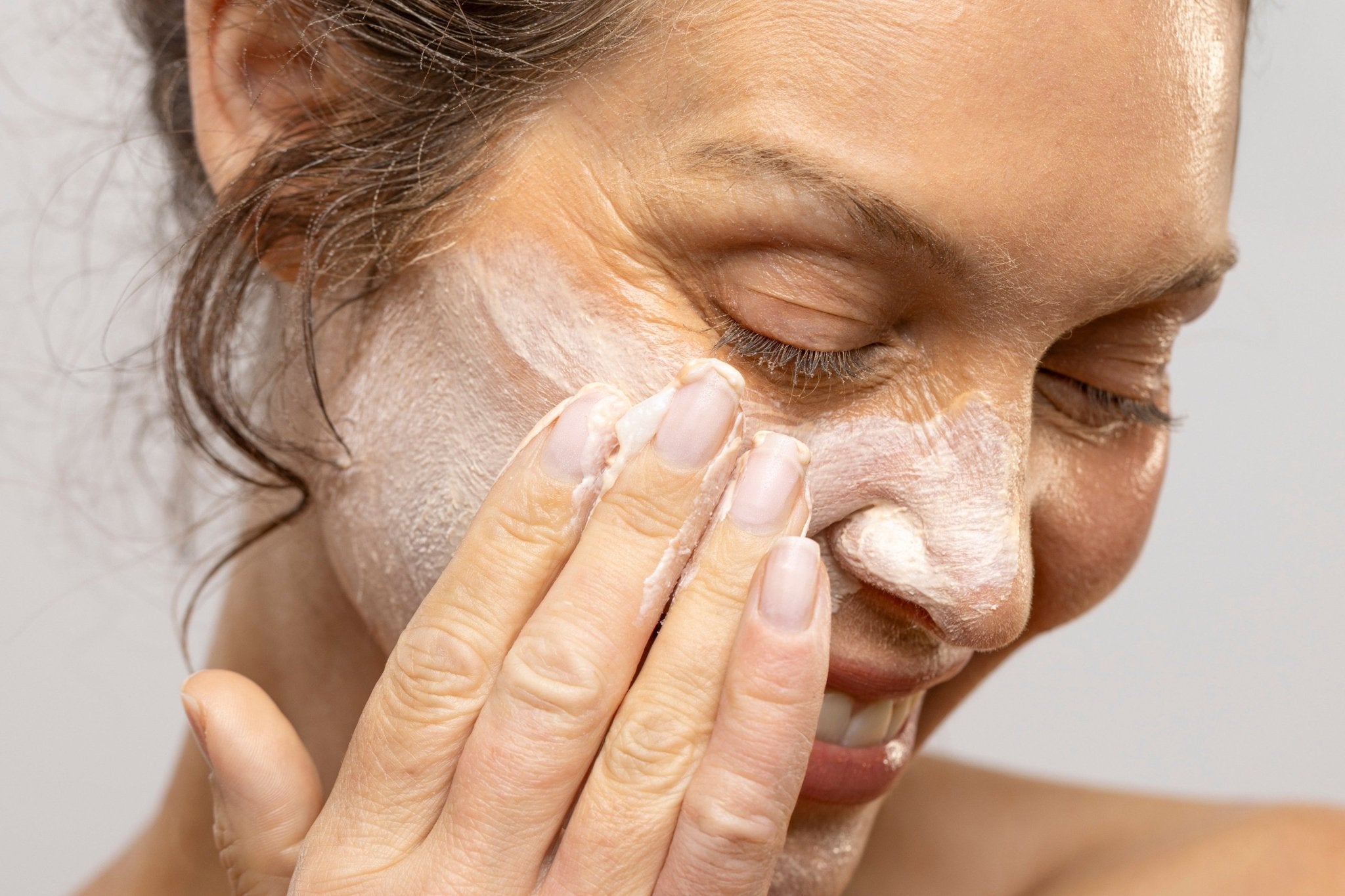 Woman applying cream to her face against a neutral background
