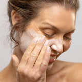 Woman applying cream to her face against a neutral background