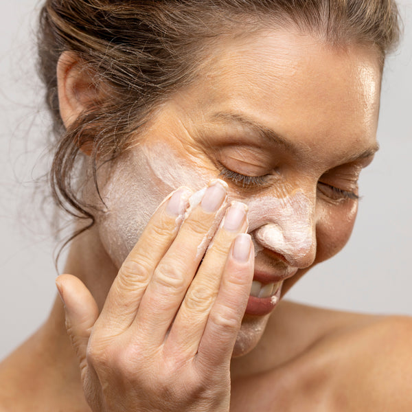 Woman applying cream to her face against a neutral background