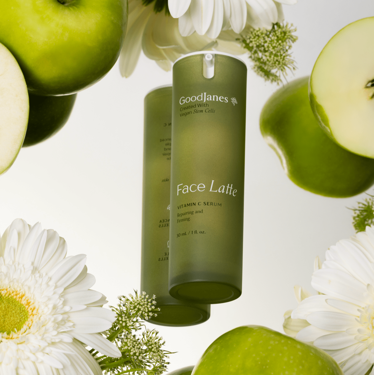 Goodlanes Face Latte bottle surrounded by green apples and white flowers on a light background
